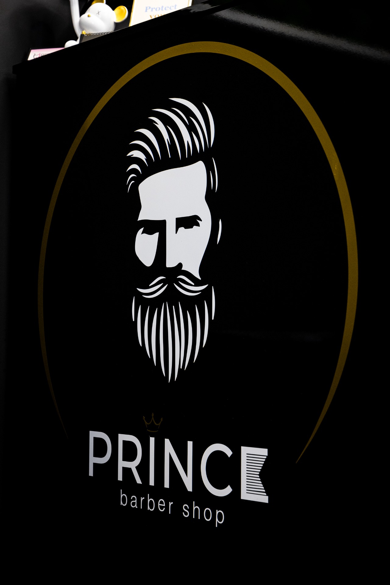 Čiernobiely siluetový portrét holiča s fúzmi a nápisom PRINCE barber shop na čiernom pozadí.